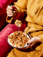 Person in red and yellow clothing holding spoon over bowl of granola cereal with milk, spoonful suspended above.