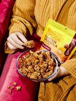 Person in mustard jacket holding bowl of peanut butter protein granola with yellow package visible.