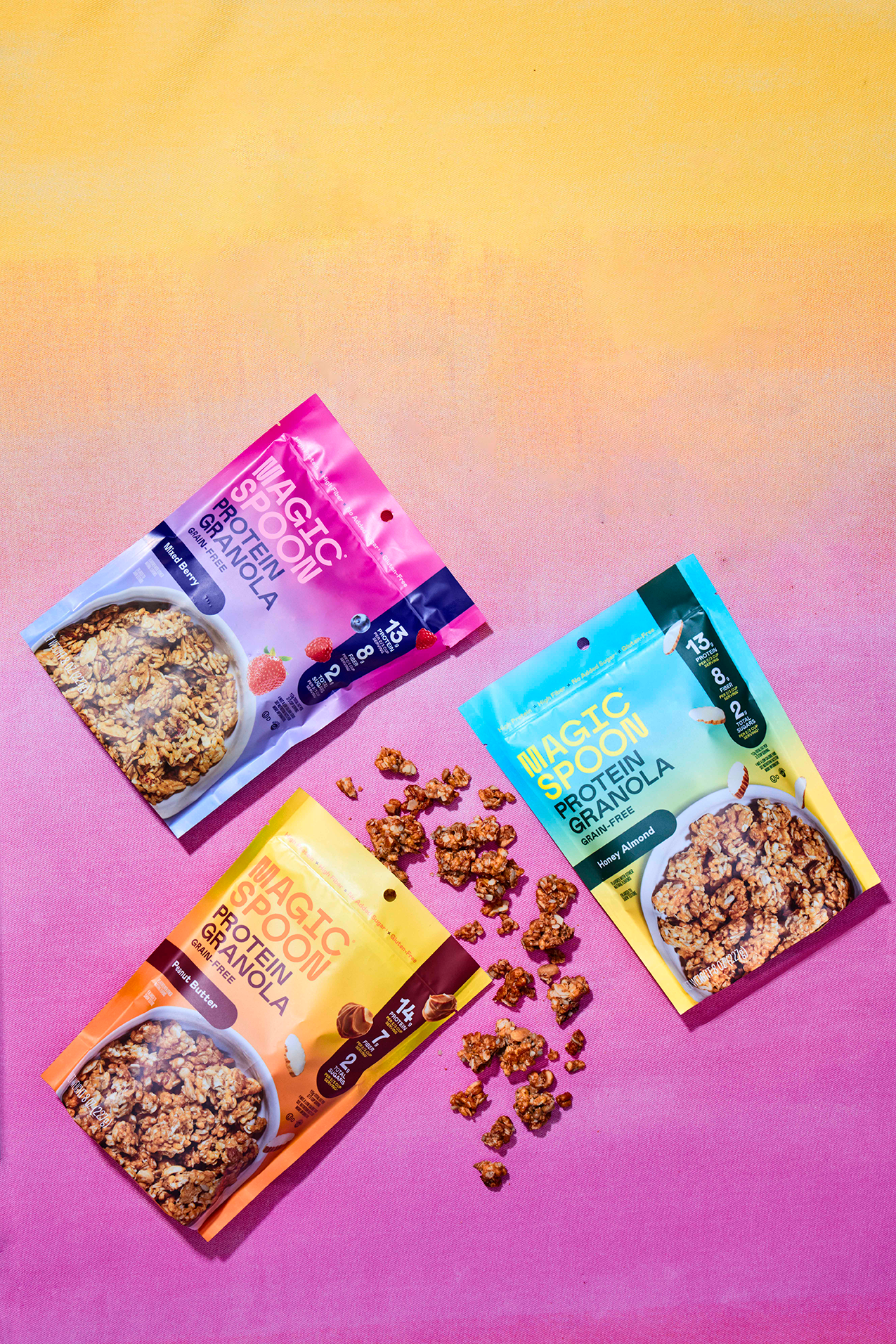 Three granola packets in honey almond, peanut butter, and mixed berry flavors displayed with loose granola clusters on a grad