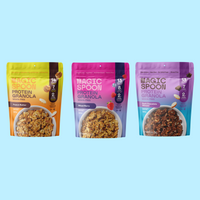 Three Magic Spoon protein granola bags in Peanut Butter, Mixed Berry, and Dark Chocolate Almond flavors on light blue backgro
